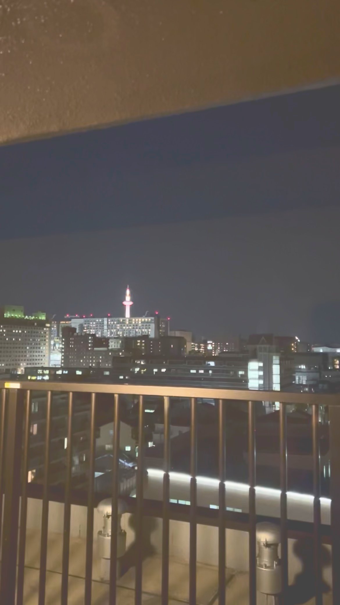バルコニーの柵越しに見える、ライトアップされた京都タワーと夜の街