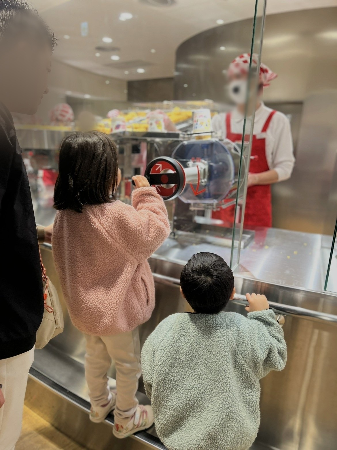 台に乗ってフィルムを包む機械のハンドルを回す子どもたち