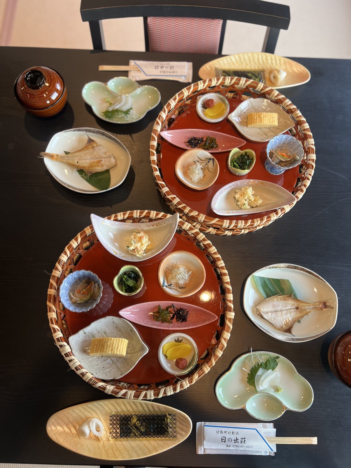 竹かごの盆に小鉢が並ぶ朝ごはん。焼き魚、お刺身、だし巻き卵など