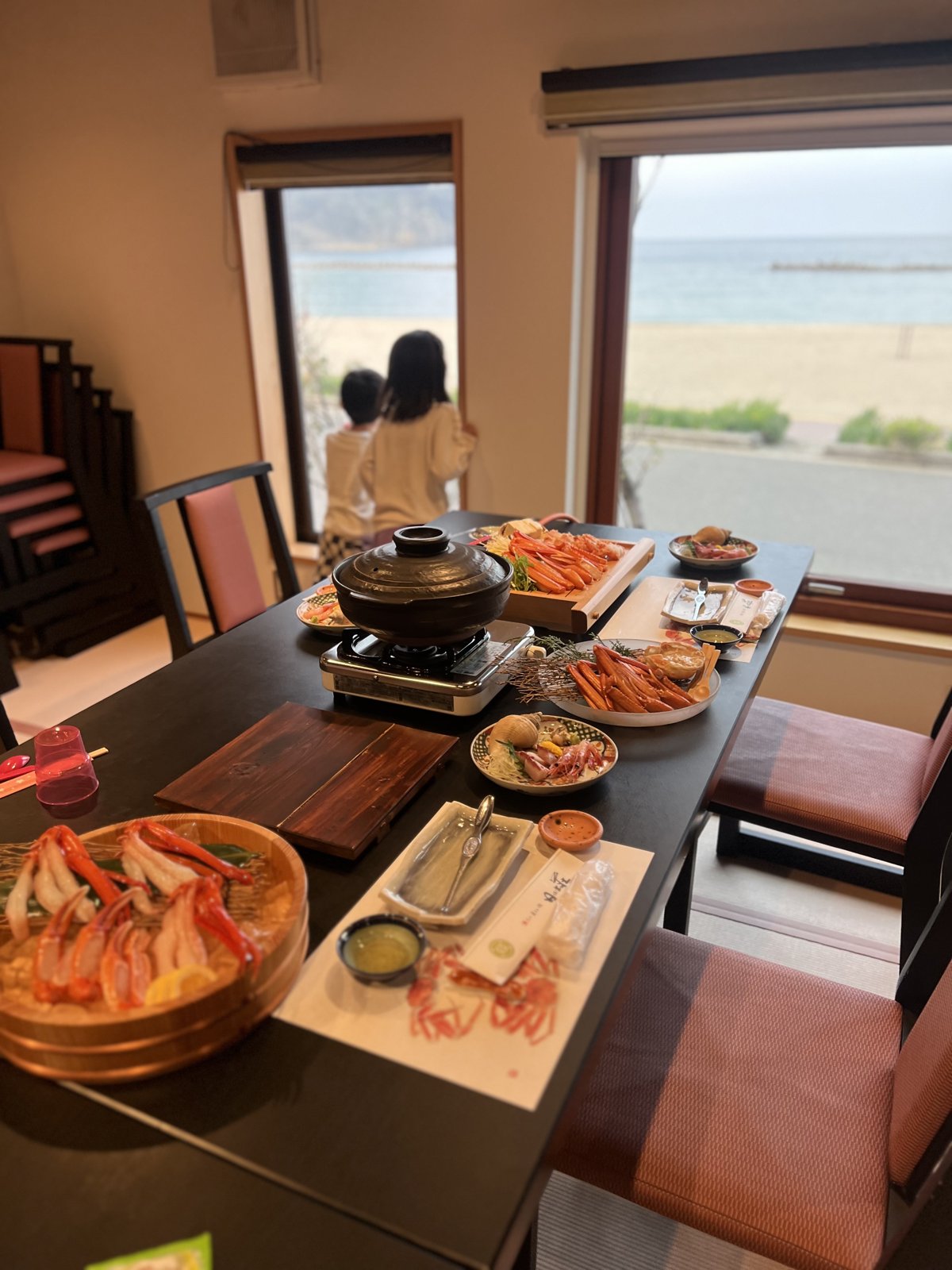テーブルいっぱいに並んだカニ料理。窓の外に竹野浜