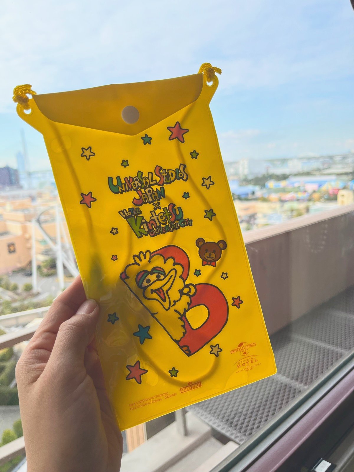 窓の外にUSJのコースターが見える部屋で、USJ×ホテル近鉄のポーチを持つ手