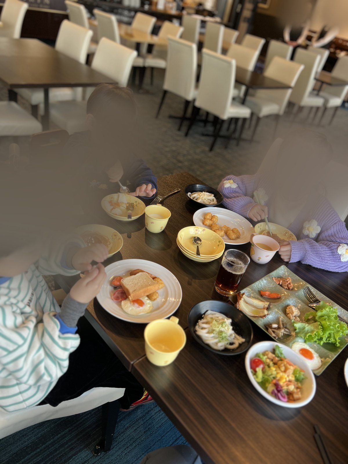パンや目玉焼き、うどん、サラダを並べて朝ごはんを食べる子どもたち。キャラクター柄の子ども用食器