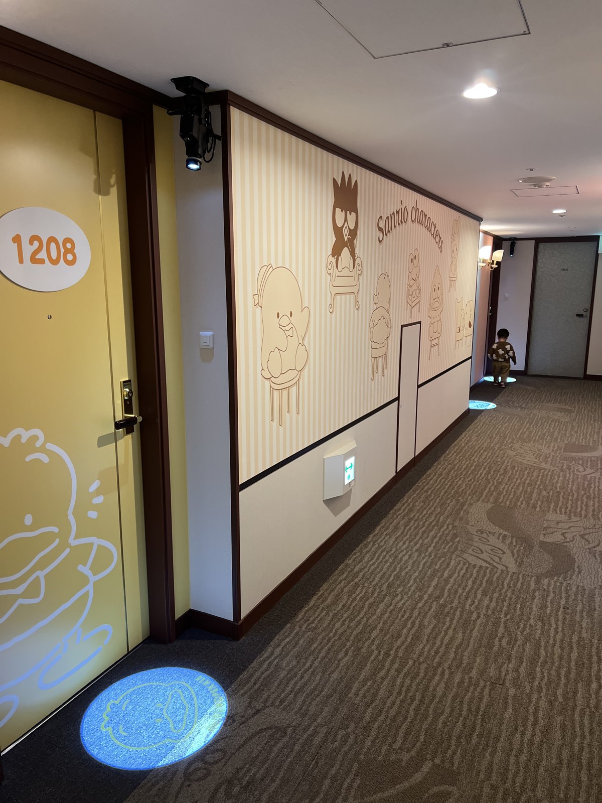 「Sanrio characters」の壁画と、ドアにキャラクターが描かれた客室前の廊下。床にもキャラクターが映し出されている