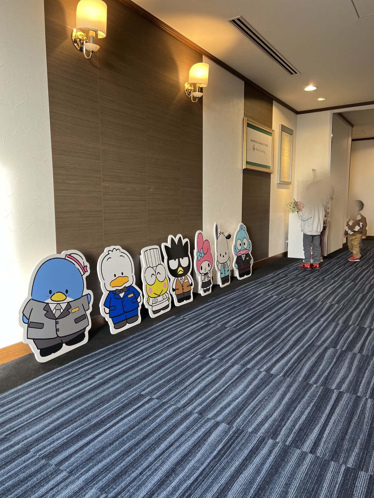 スーツやコック帽姿のサンリオキャラクターのパネルが並ぶ廊下