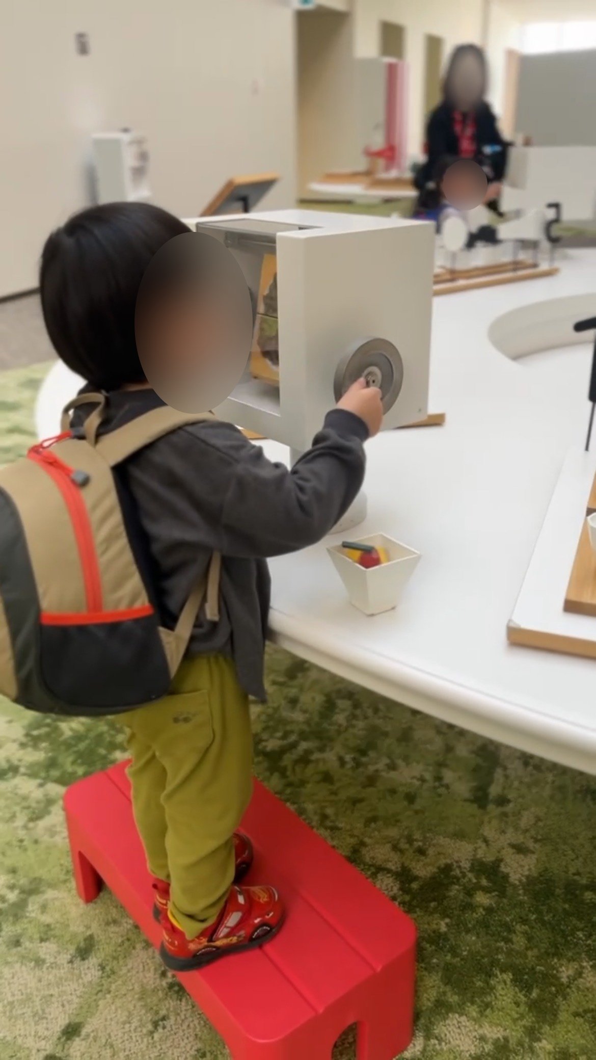 踏み台に立って展示のハンドルを回す子ども