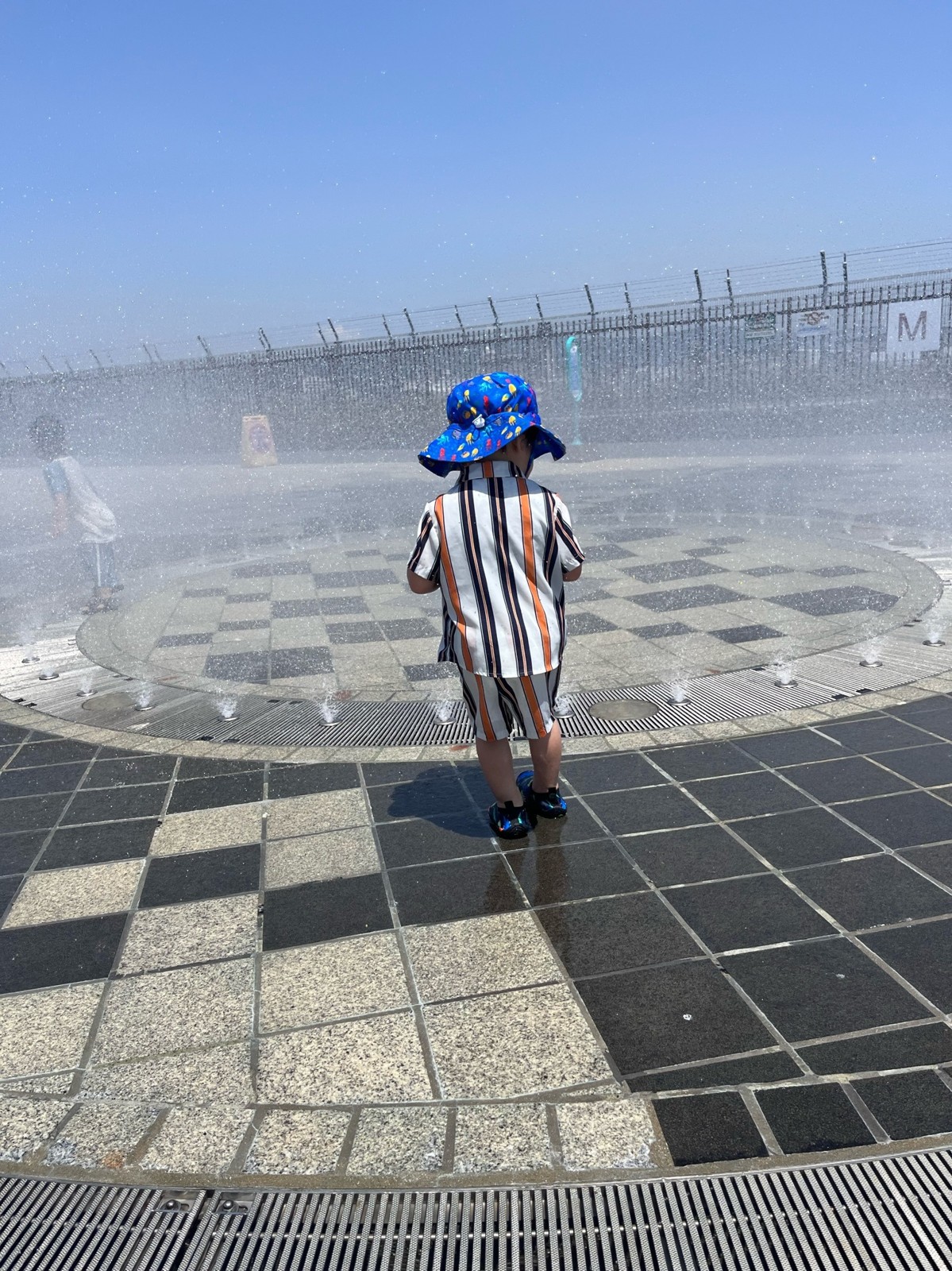 噴水の水しぶきの前に立つ子ども