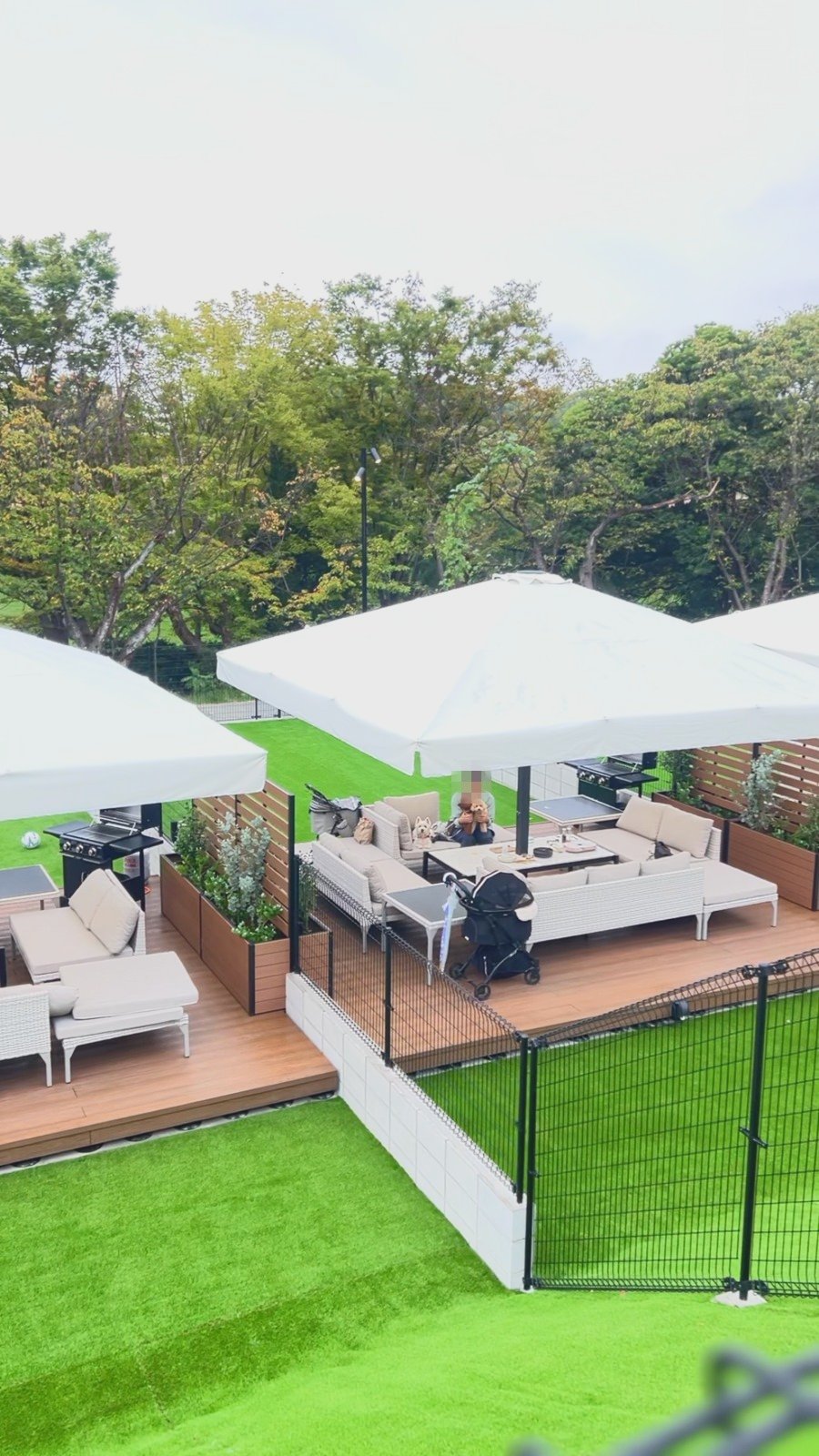 人工芝のドッグランに面したウッドデッキのソファ席とパラソル、グリル