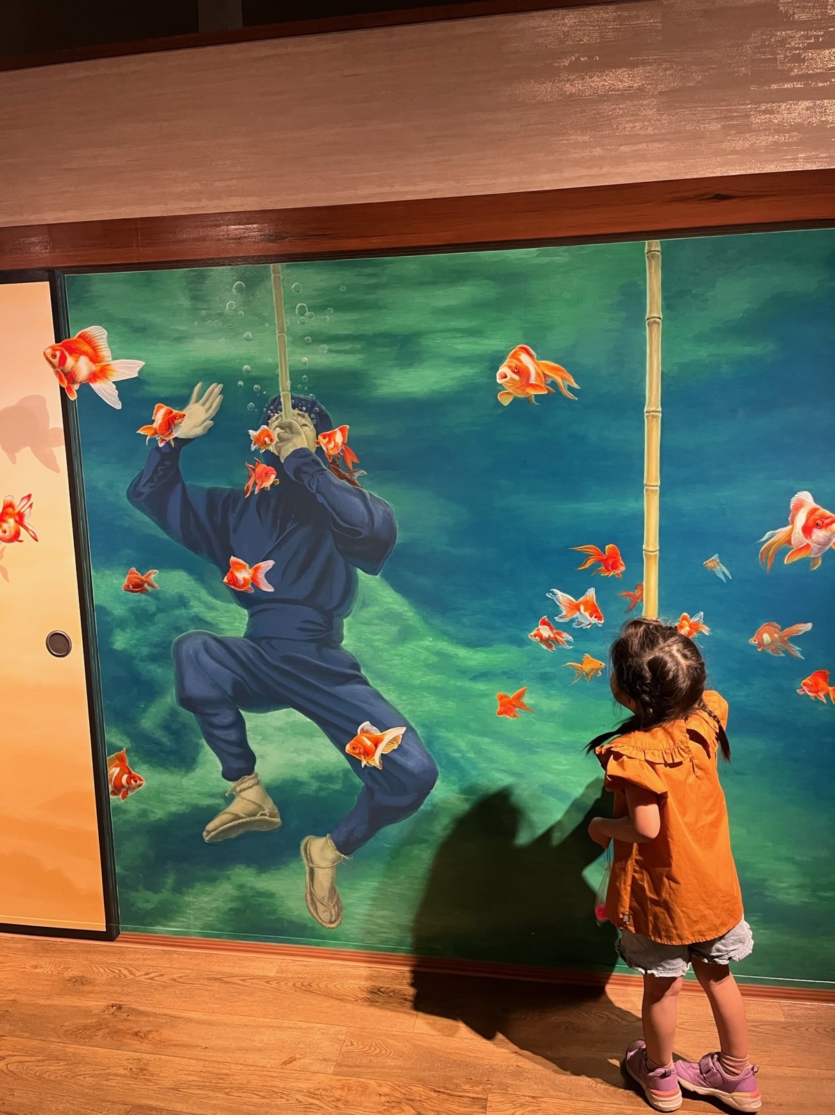 金魚が泳ぐ襖絵の前に立つ子ども