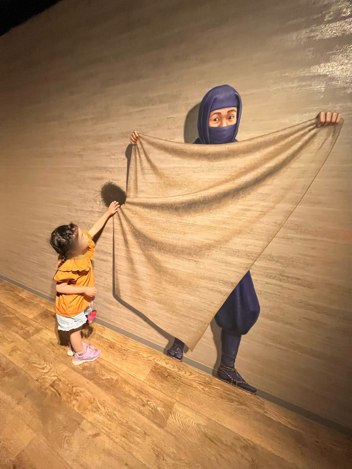 忍者が広げた布のトリックアートに手を伸ばす子ども