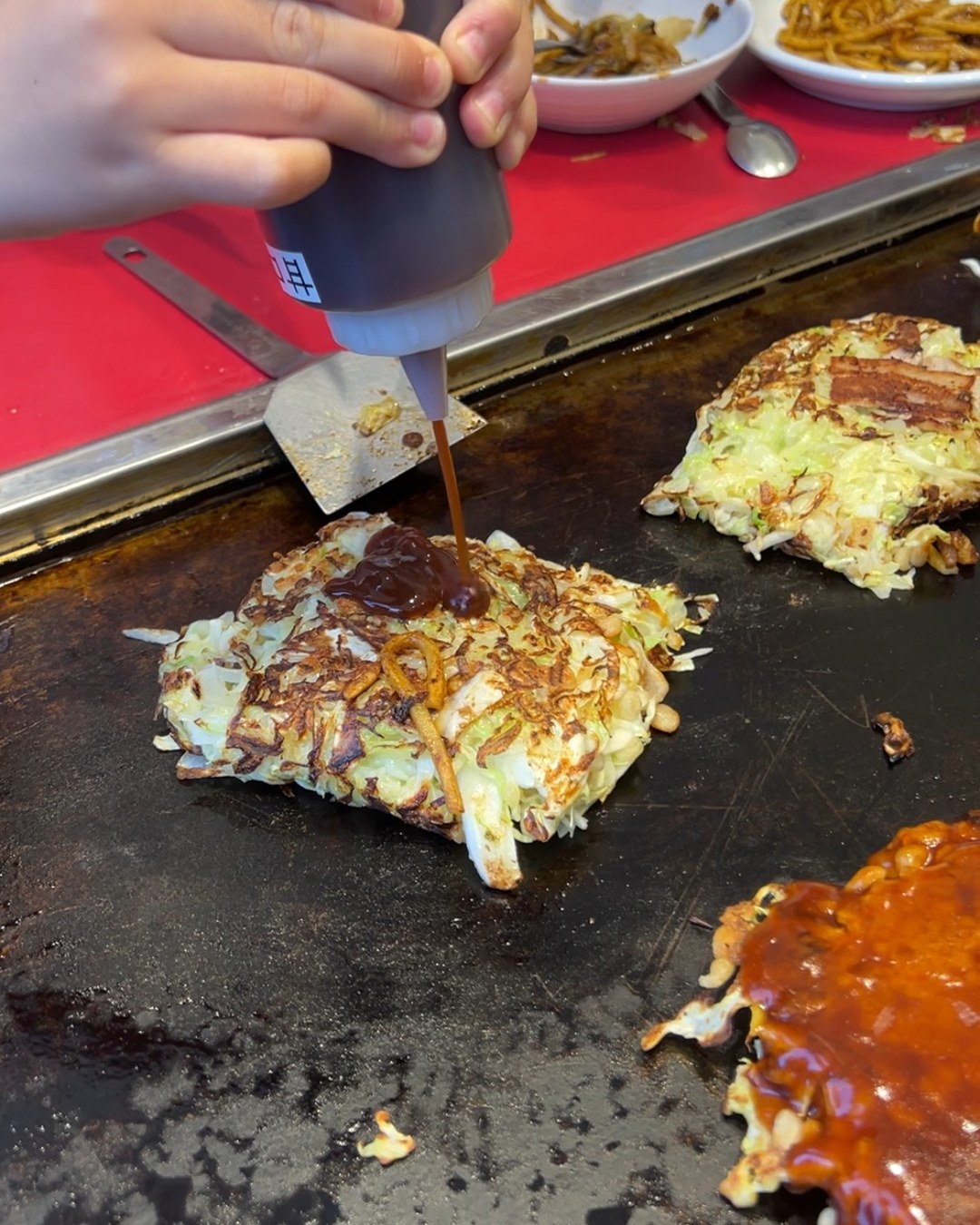 鉄板のお好み焼きにソースをかけているところ