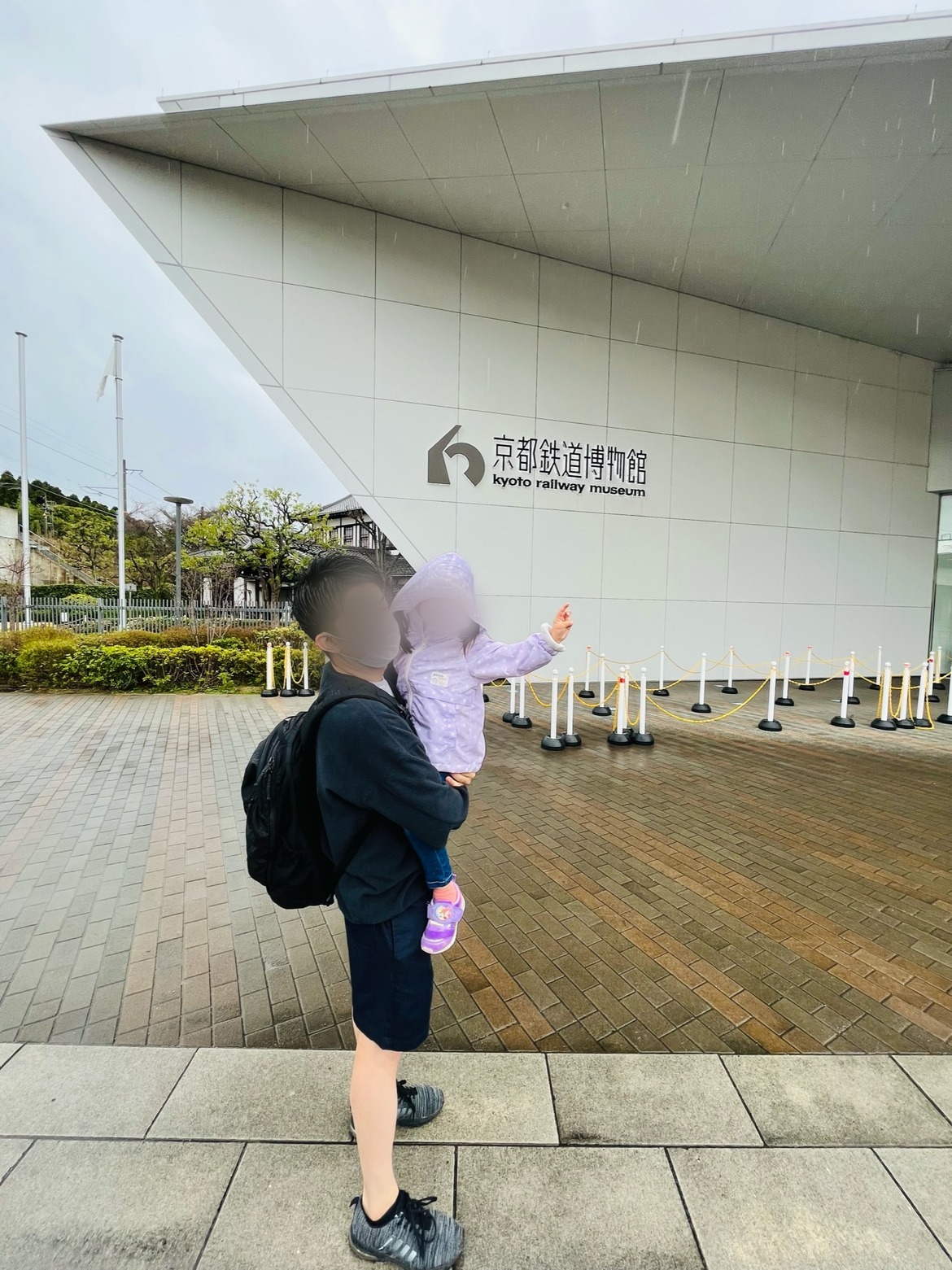 「京都鉄道博物館」の看板の前で子どもを抱っこする