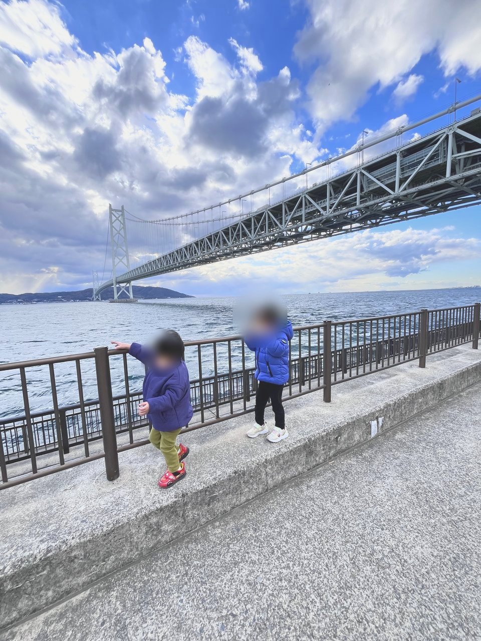 海ぞいの低い塀の上を歩く子どもたち。奥に明石海峡大橋