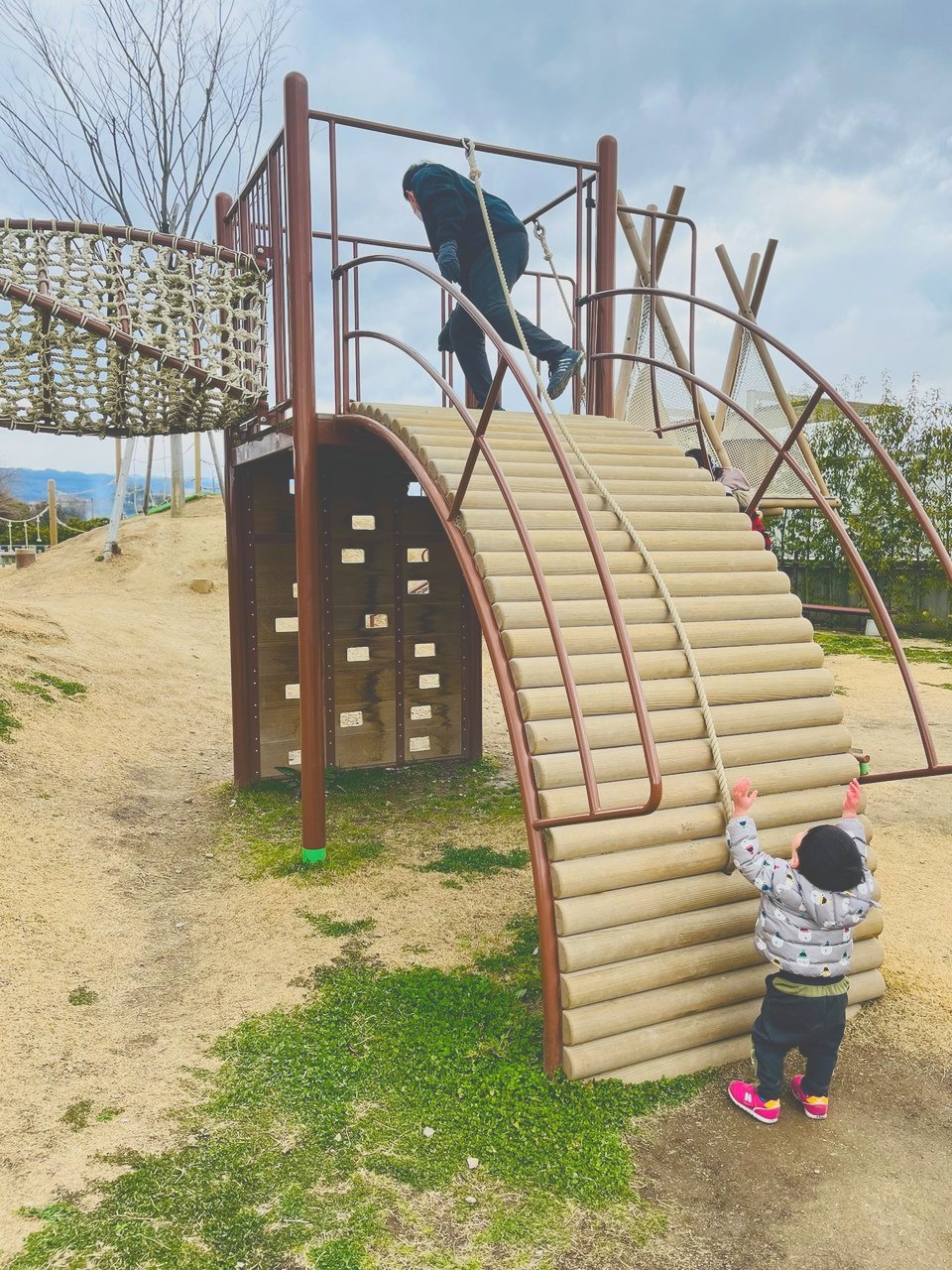 丸太を並べたアーチ形の坂と、それを見上げる子ども