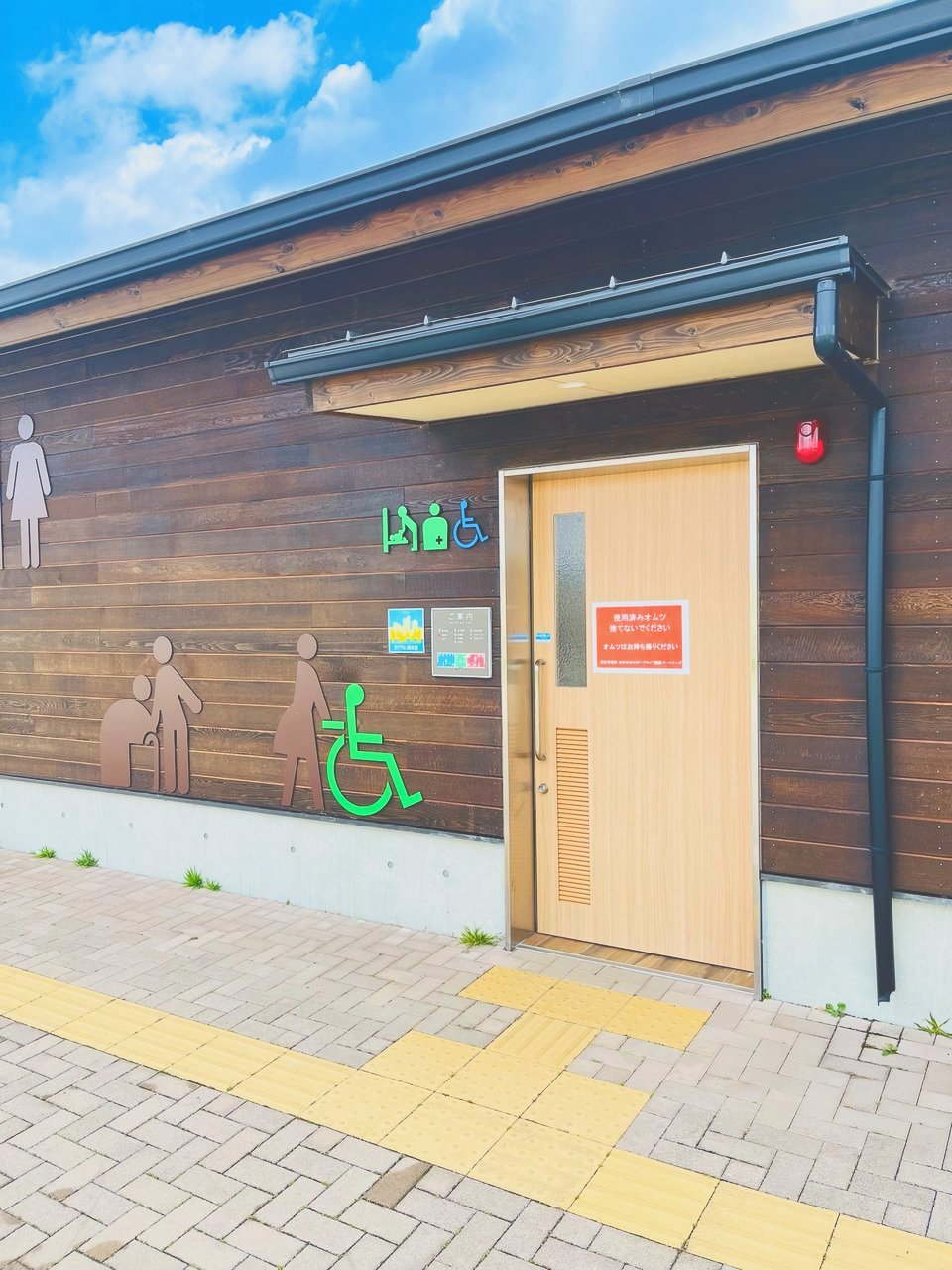 木の外壁のトイレの建物。入口の横におむつ替えなどのマーク