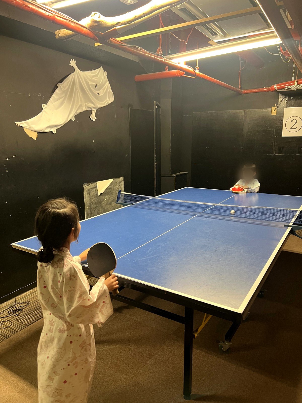 妖怪の飾りがある卓球コーナーで、浴衣姿で卓球をする娘と息子