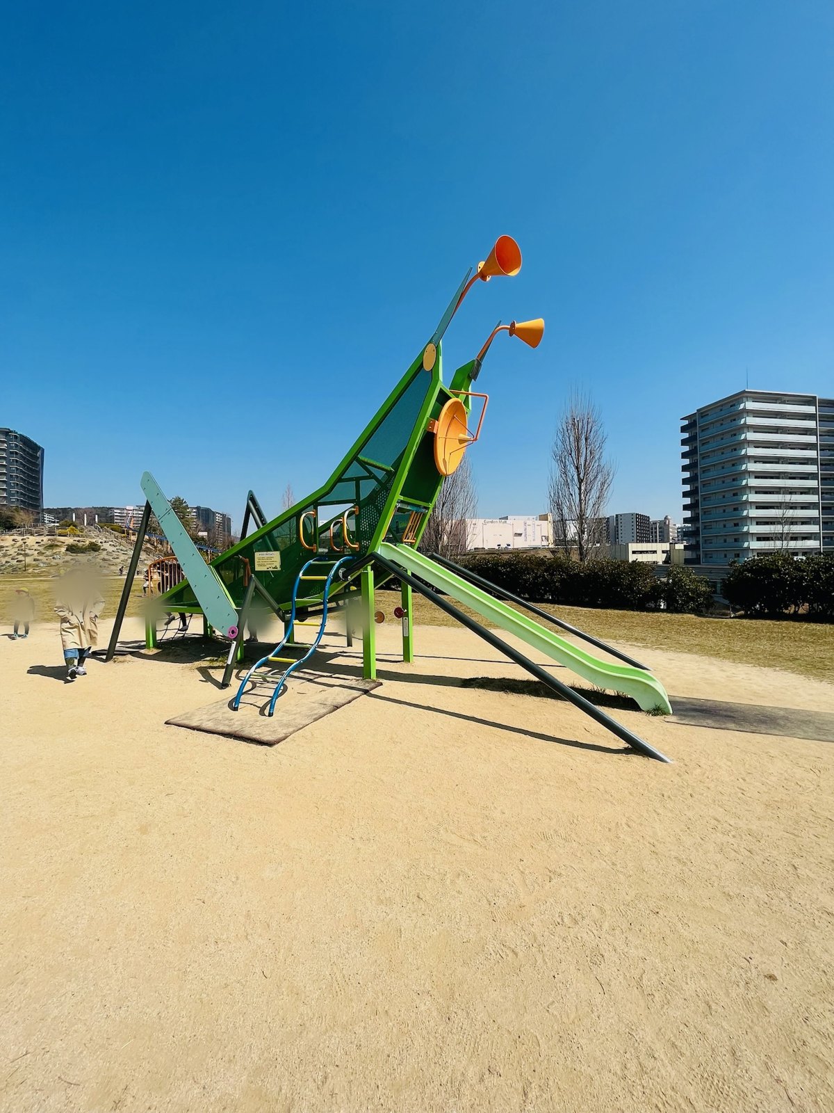大きなバッタの形をした遊具。おなかの部分から緑のすべり台が伸びている