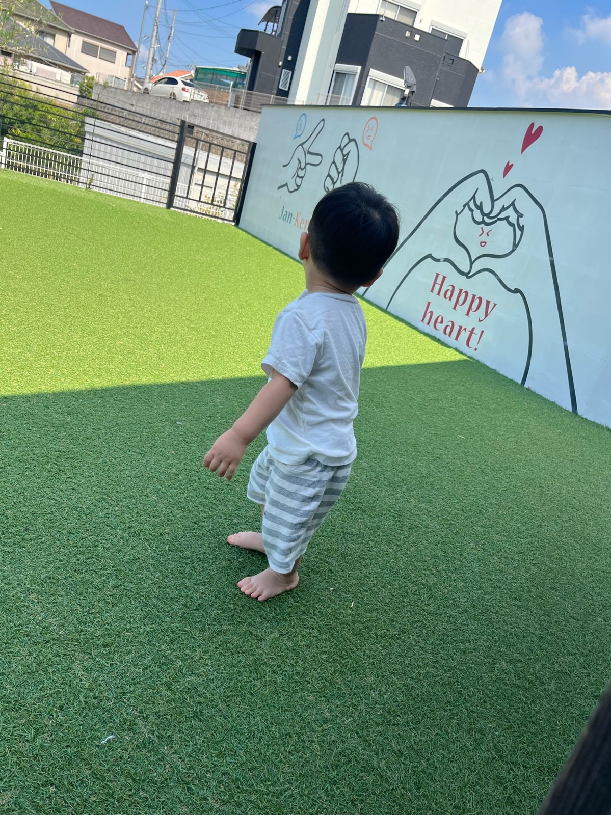 壁に絵が描かれた人工芝の広場を歩く子ども