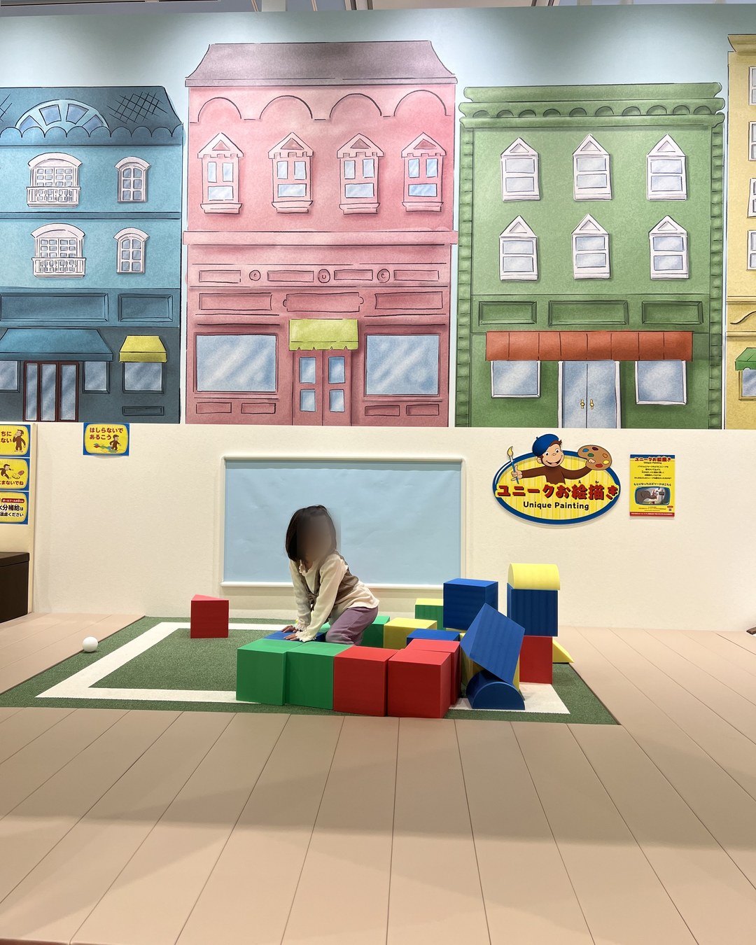 街並みの壁画の前で大きなスポンジブロックを積む子ども