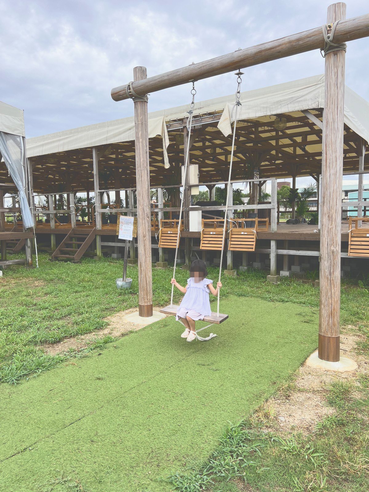 芝生に立つ木製のブランコに乗る子ども
