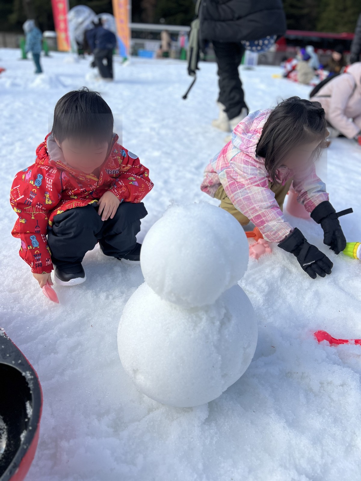 雪玉をふたつ重ねて雪だるまを作る子どもたち