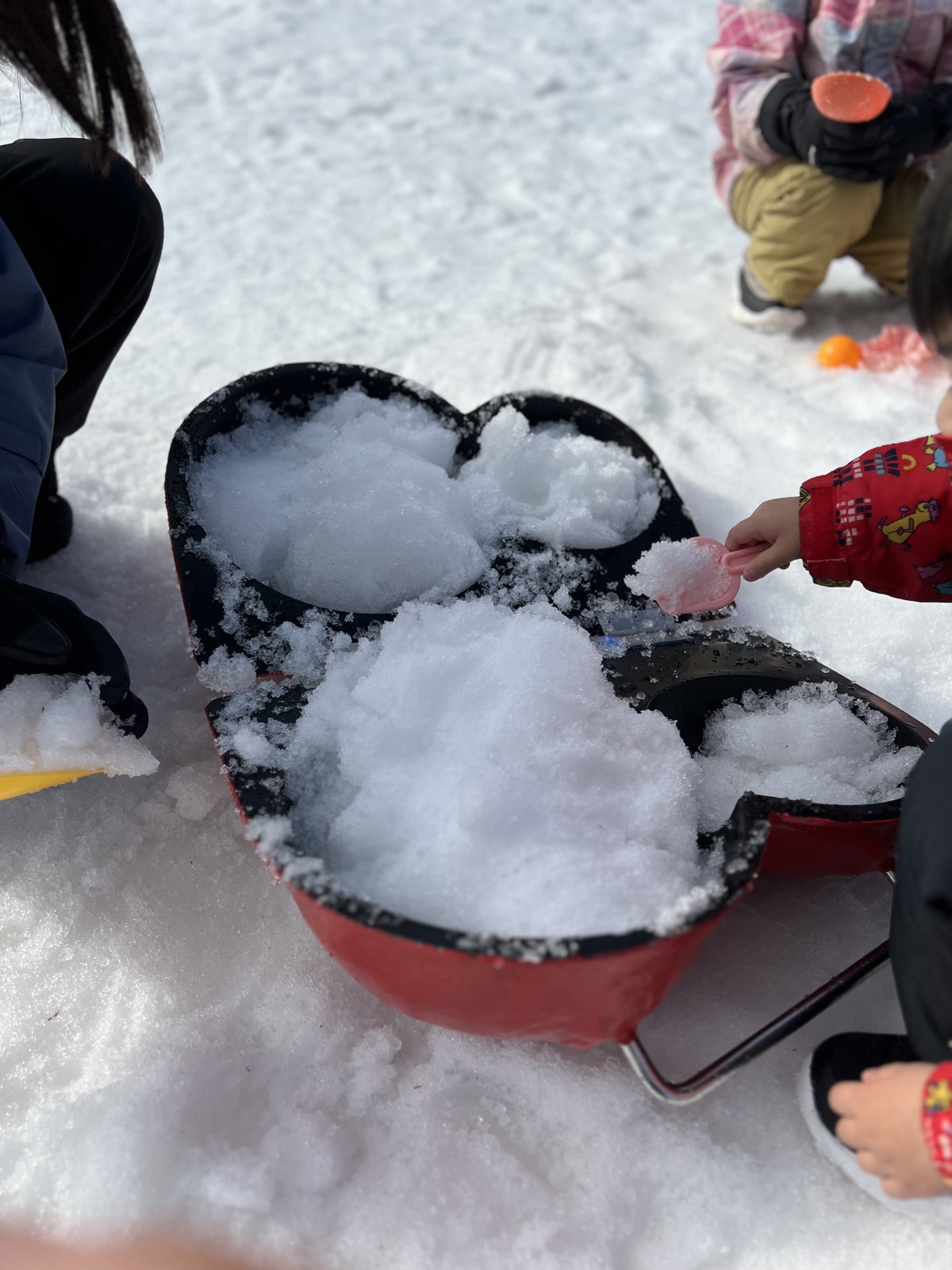 雪だるまの形をした型に雪を詰める子ども