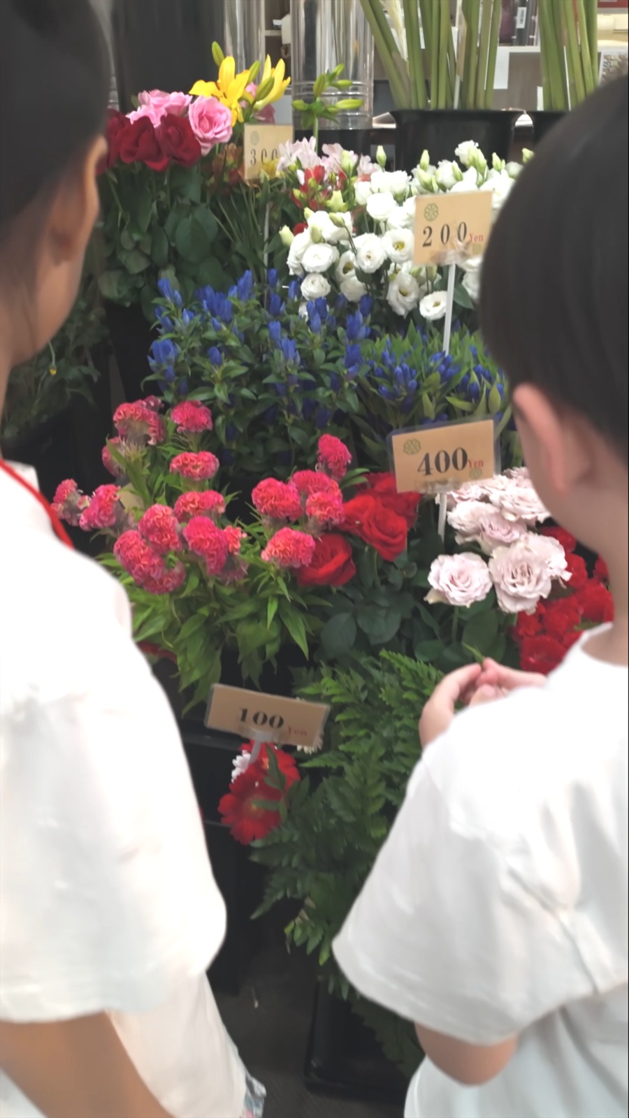 値札の立った花が並ぶ店先を見る子どもたち