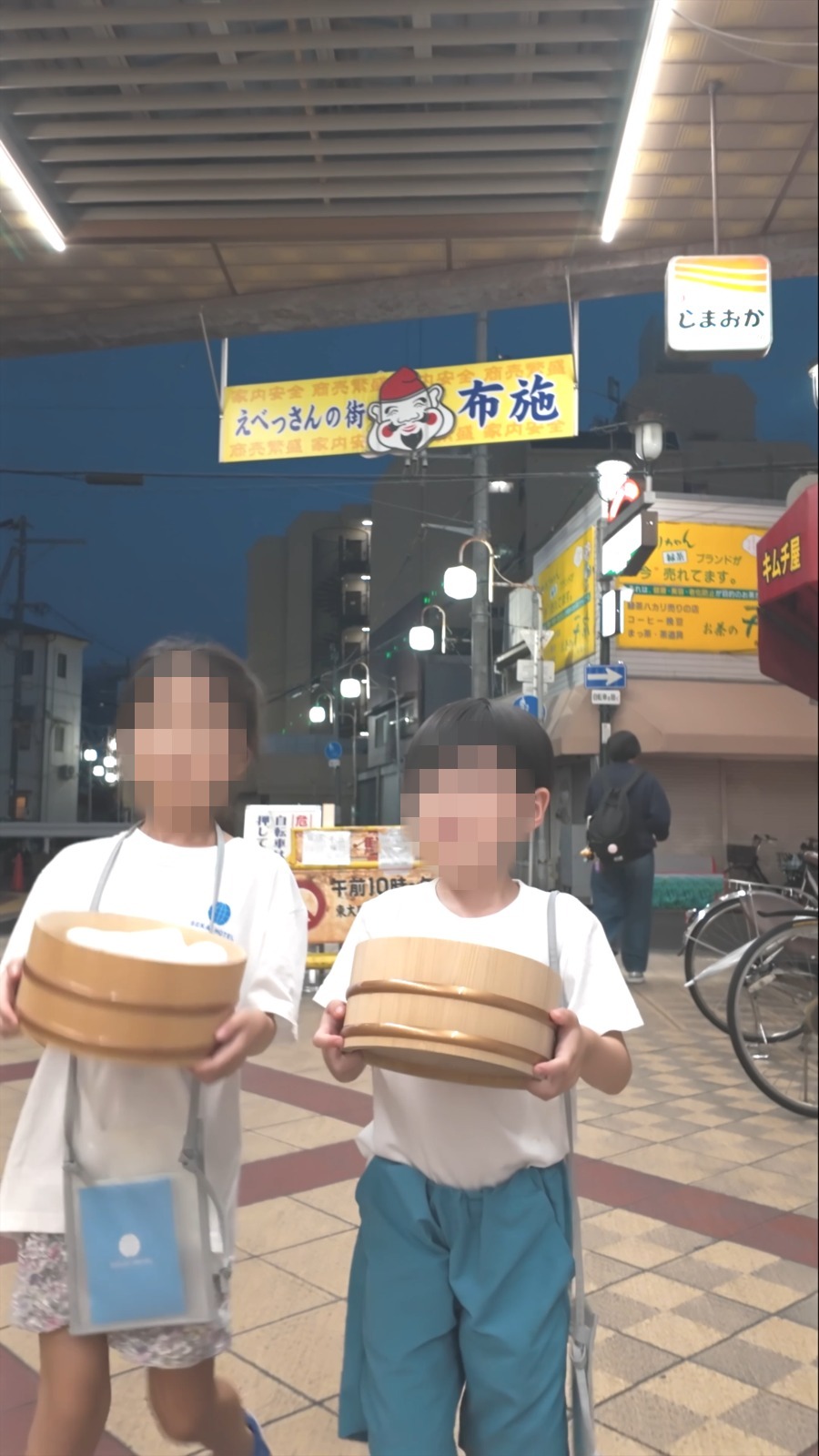 夜の商店街でおけを持つ子どもたち