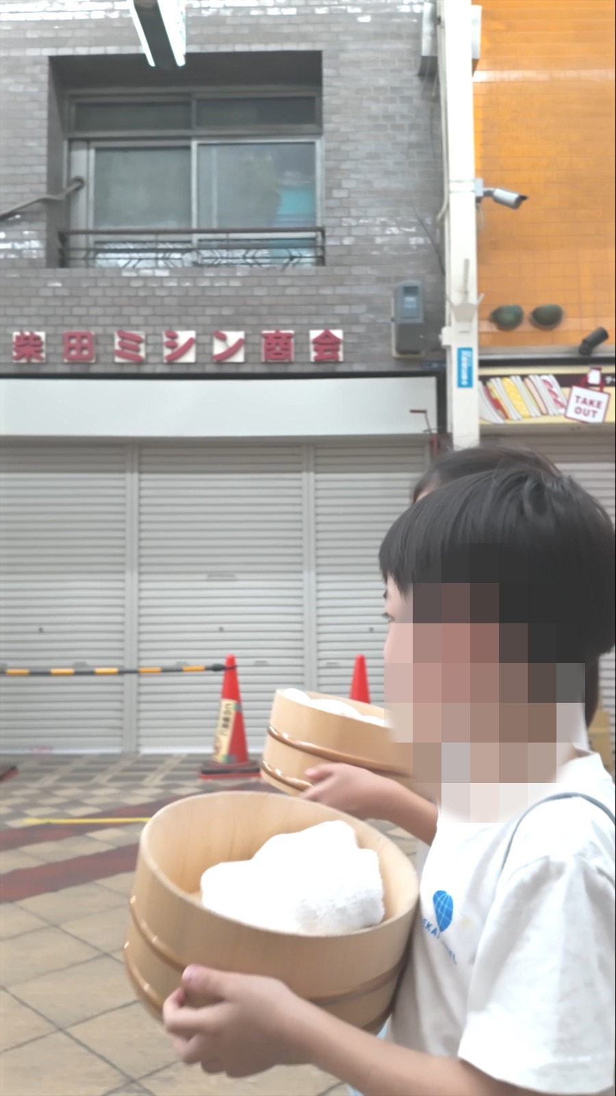 おけを抱えて商店街を歩く子ども