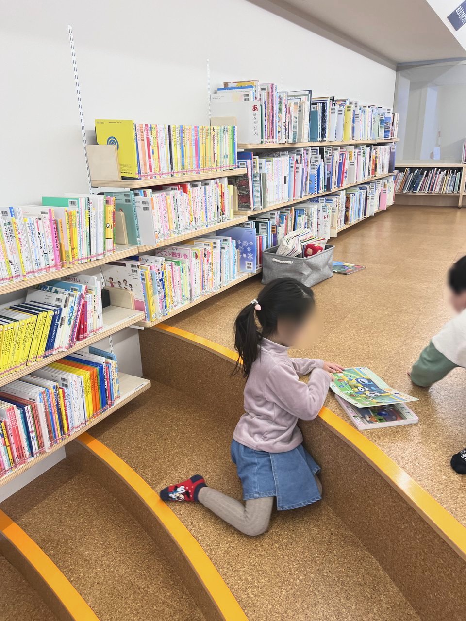 階段状の床で寝転ぶように絵本を読む子どもたち