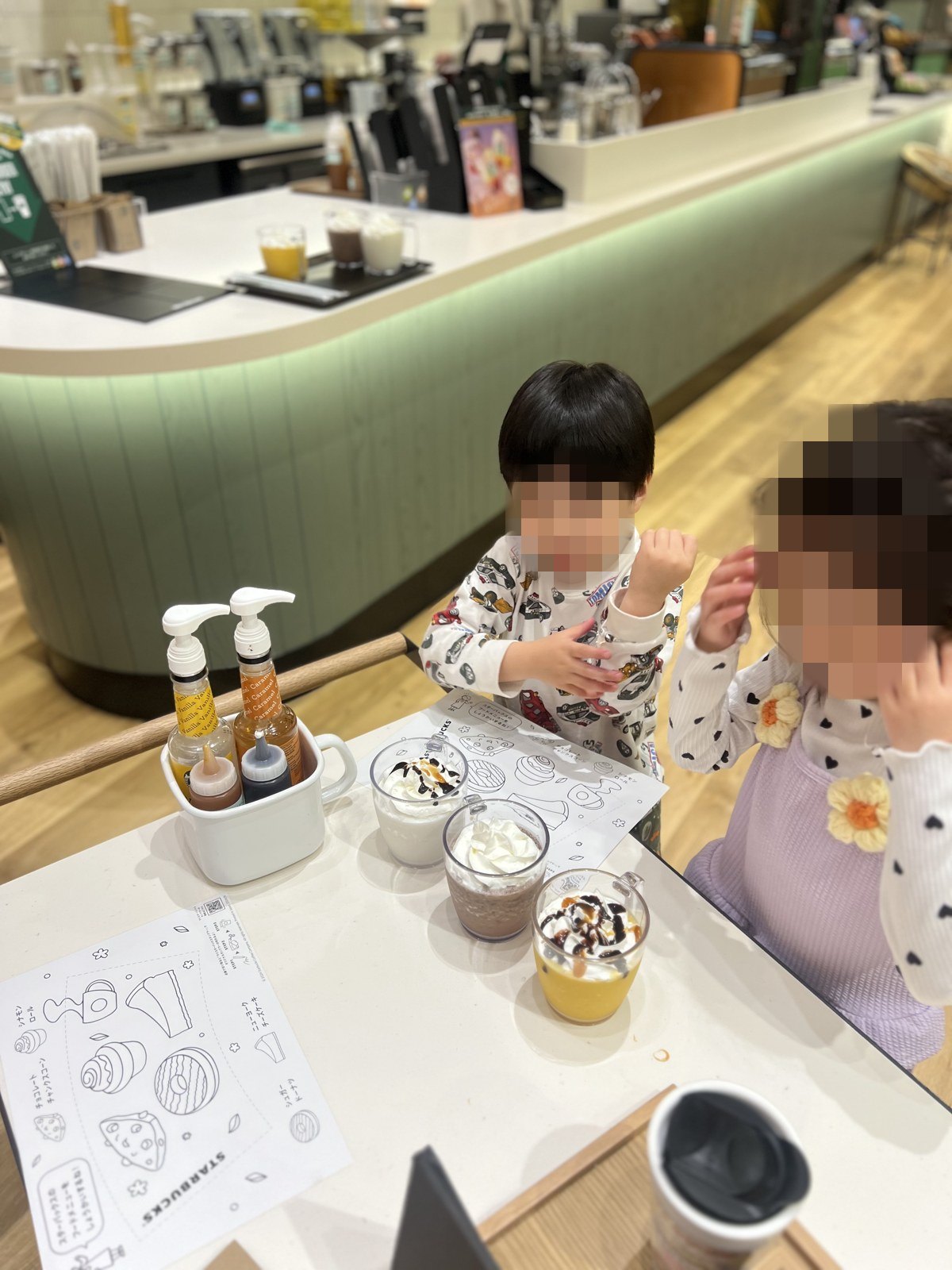 テーブルでぬりえと飲み物を前にする子どもたち
