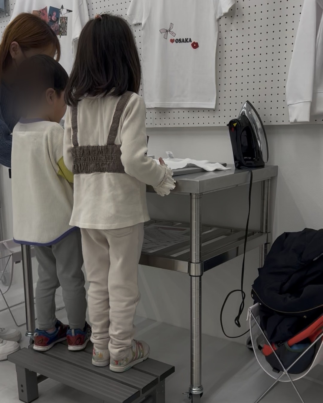 踏み台に乗ってアイロン作業を見ている子どもたち