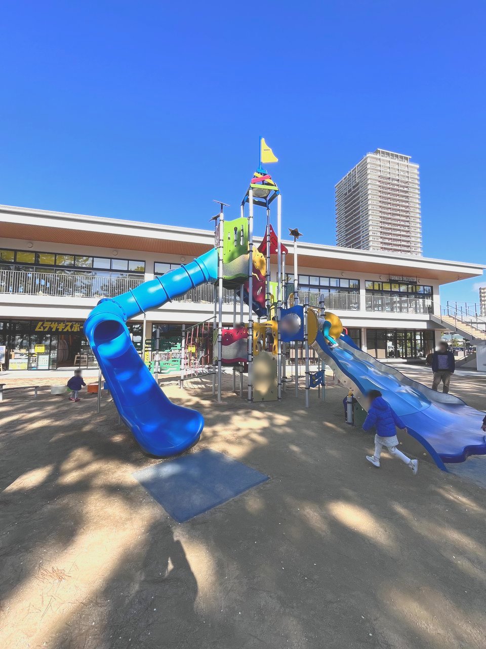 すべり台がいくつもついた大きな遊具。奥に白い建物