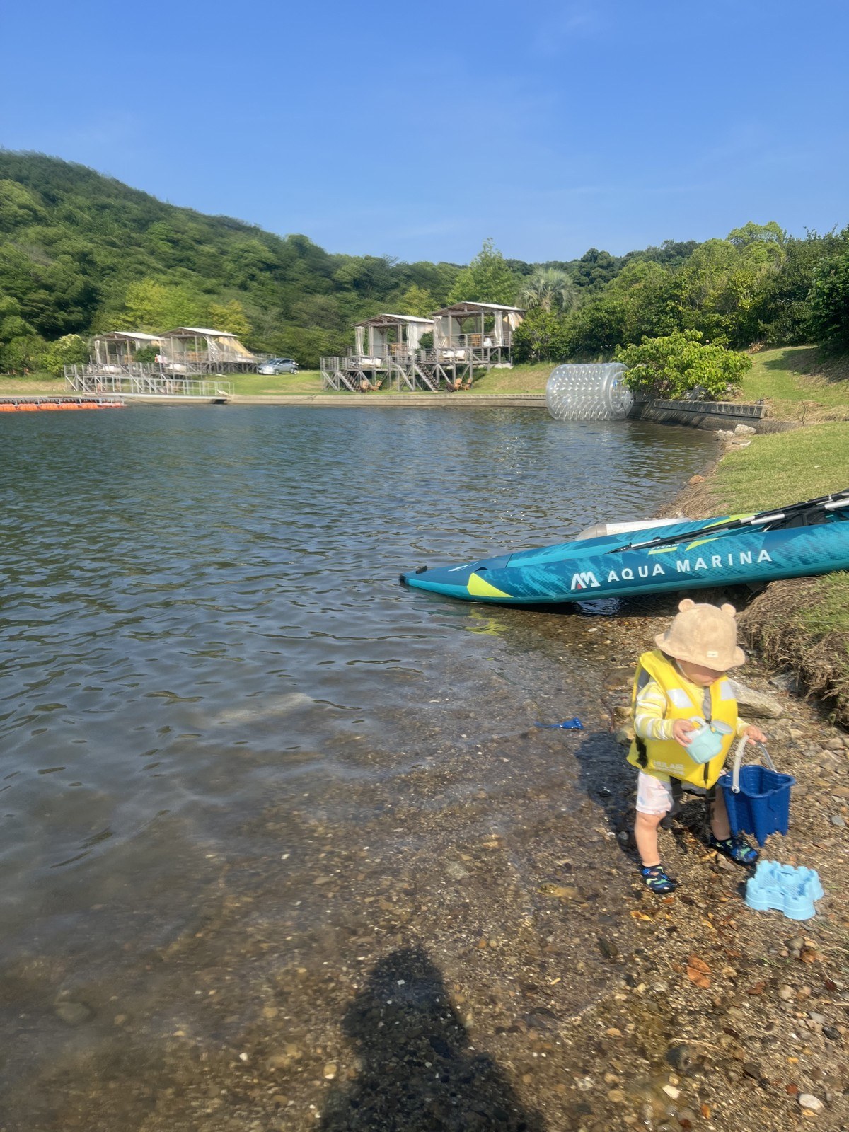 水際にしゃがんで遊ぶ、ライフジャケットを着た小さい子