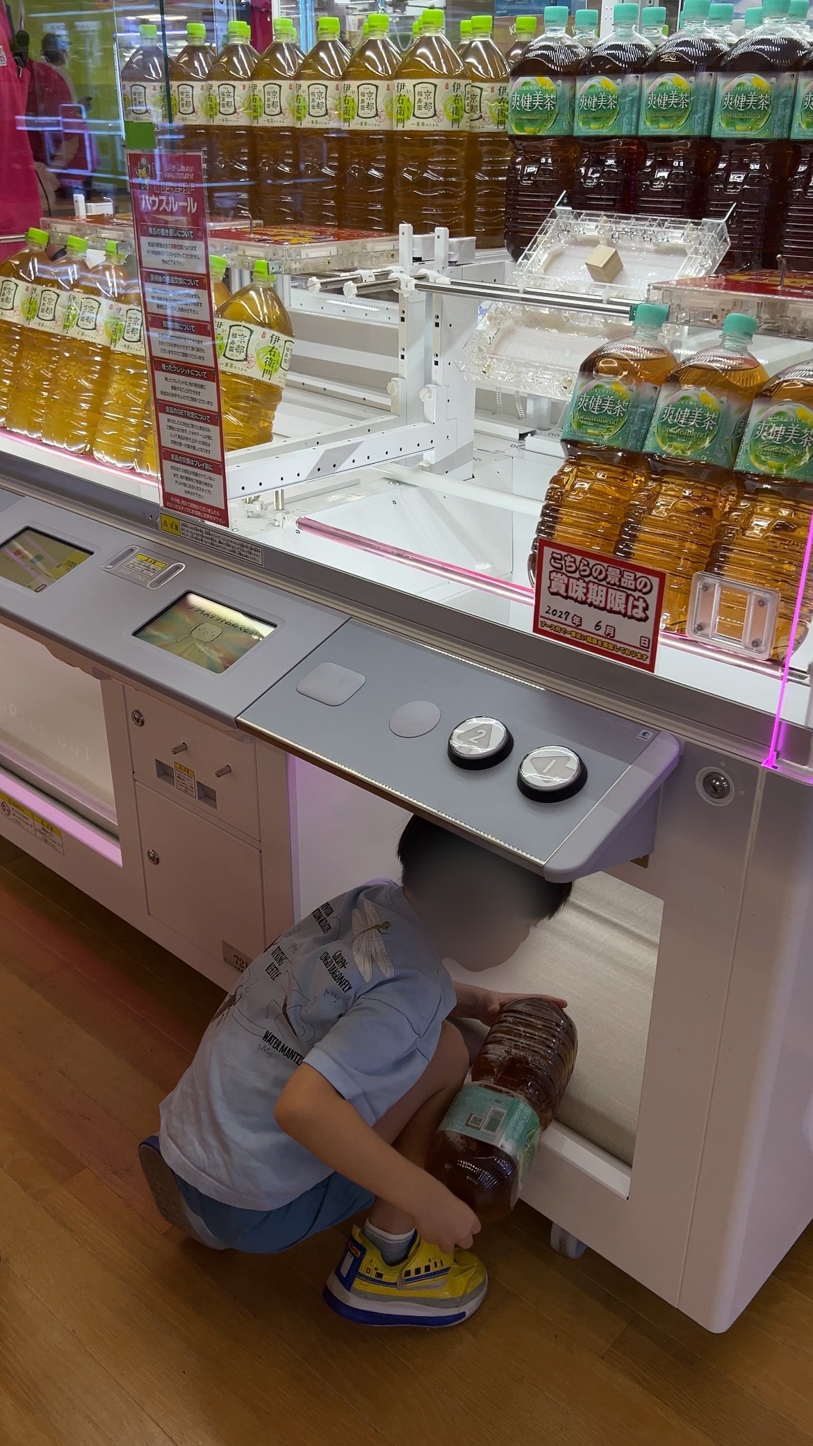 2リットルのお茶を取り出し口から抱えて出す子ども