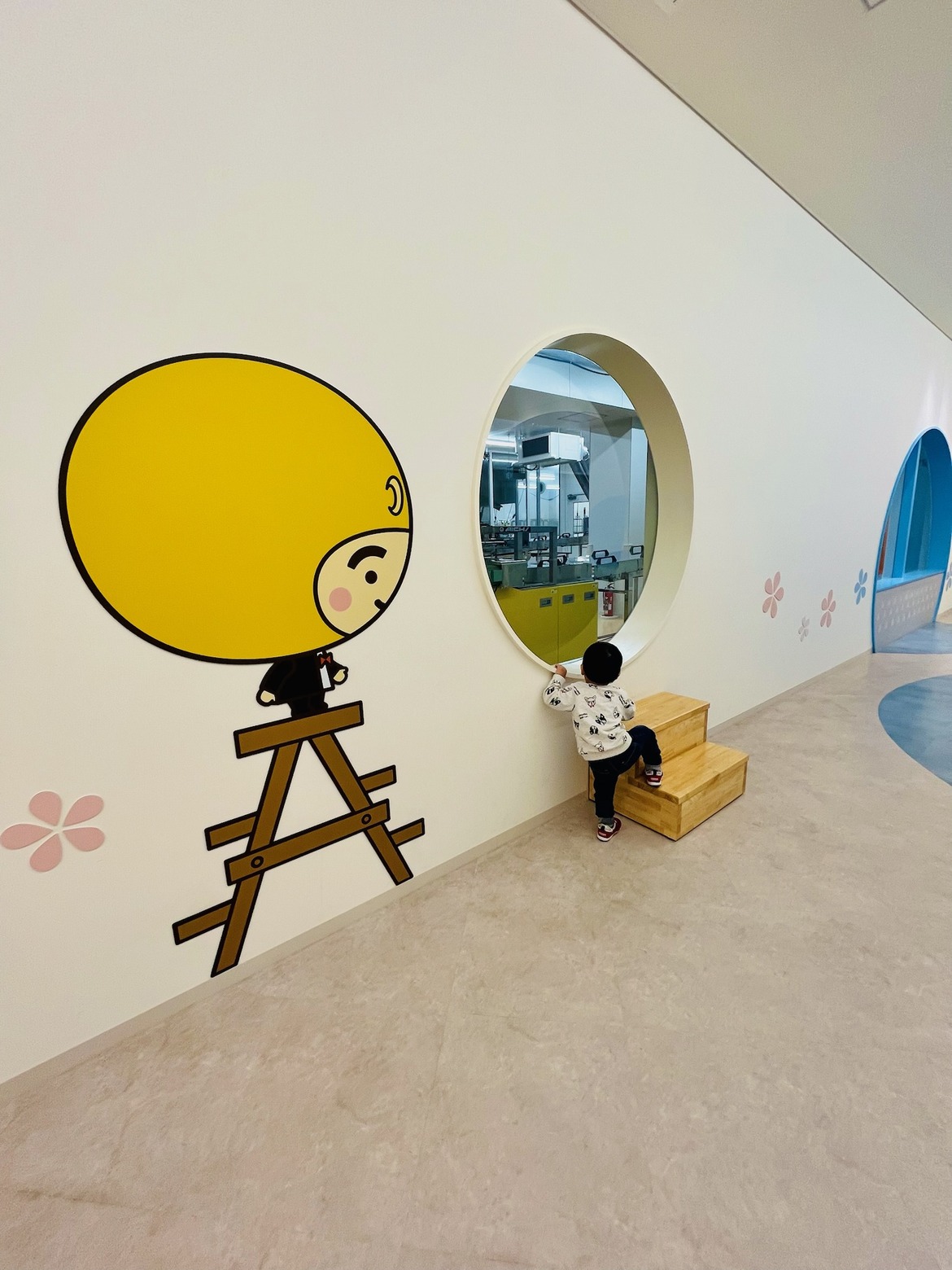 丸くくり抜かれた窓から工場をのぞく子ども