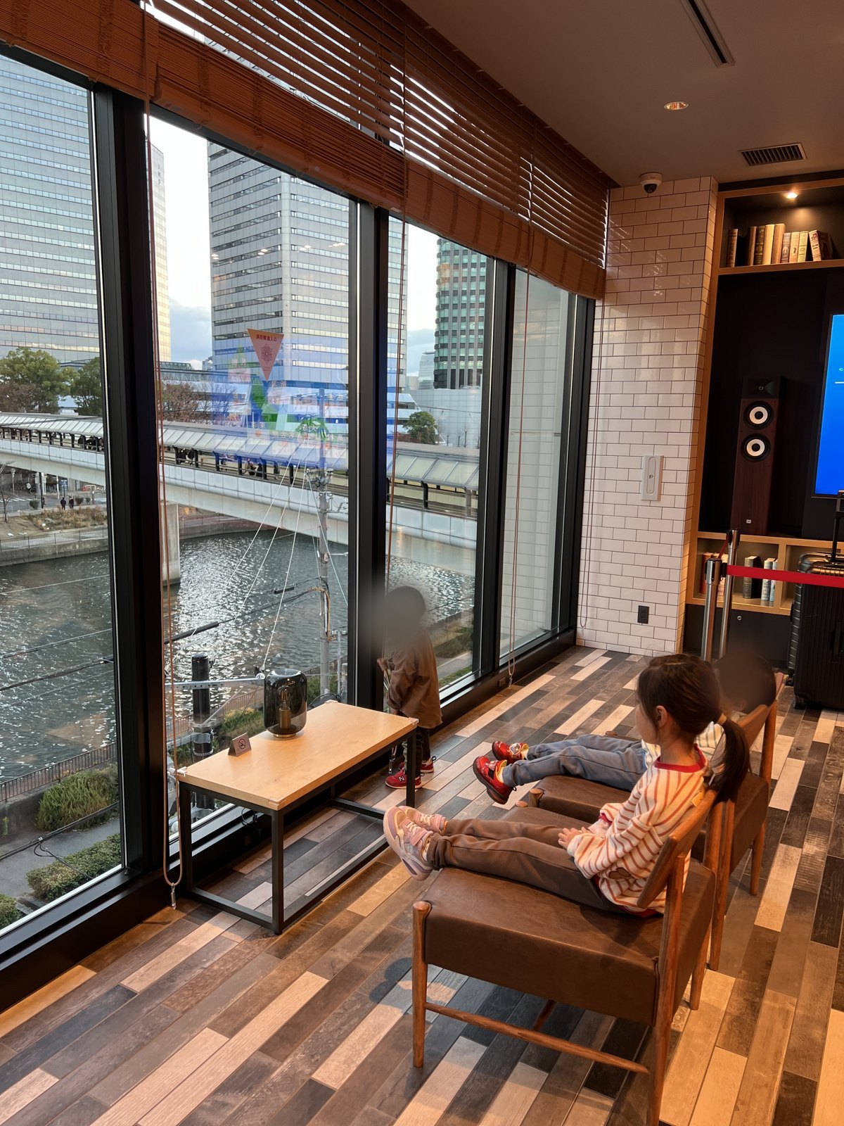 大きな窓から川とビル街が見える館内の席で、景色を眺める子どもたち